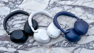 Black, white and blue models of the Sony WH-1000XM6 noise-cancelling headphones on a marble table