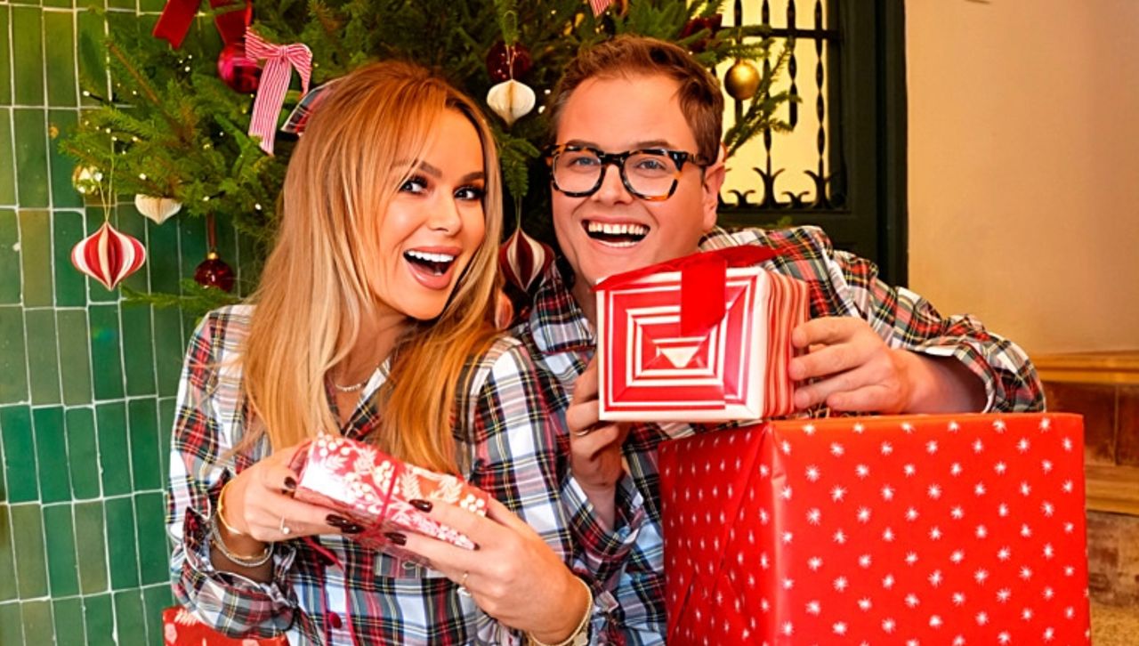 A blonde woman and brown haired man in glasses exchange Christmas gifts in pyjamas