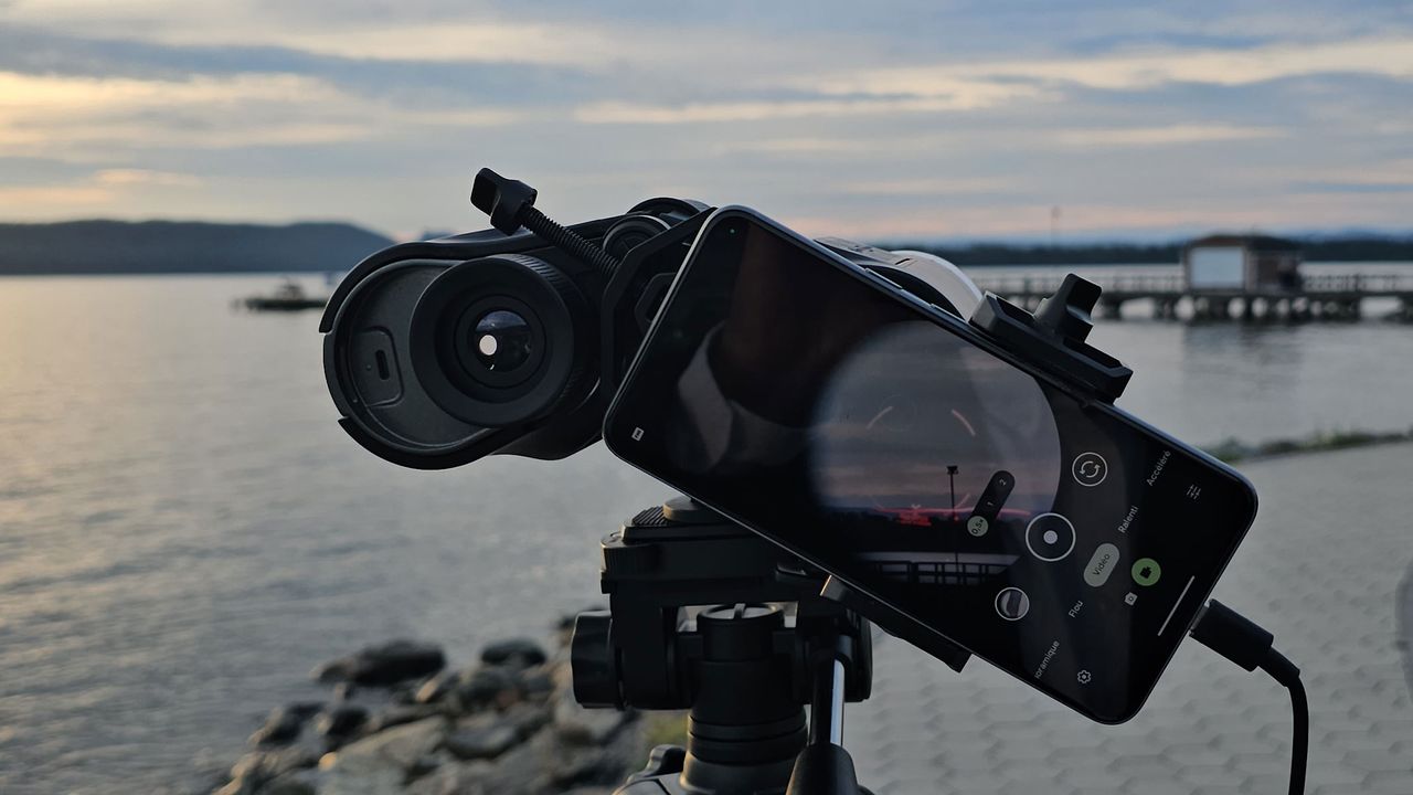 A smartphone showing the view through the Unistellar Envision binoculars with a red AR overlay of the landscape with a lake in the background.