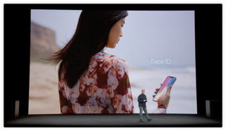 A person holds an iPhone and looks at Face ID on its screen to unlock the device.