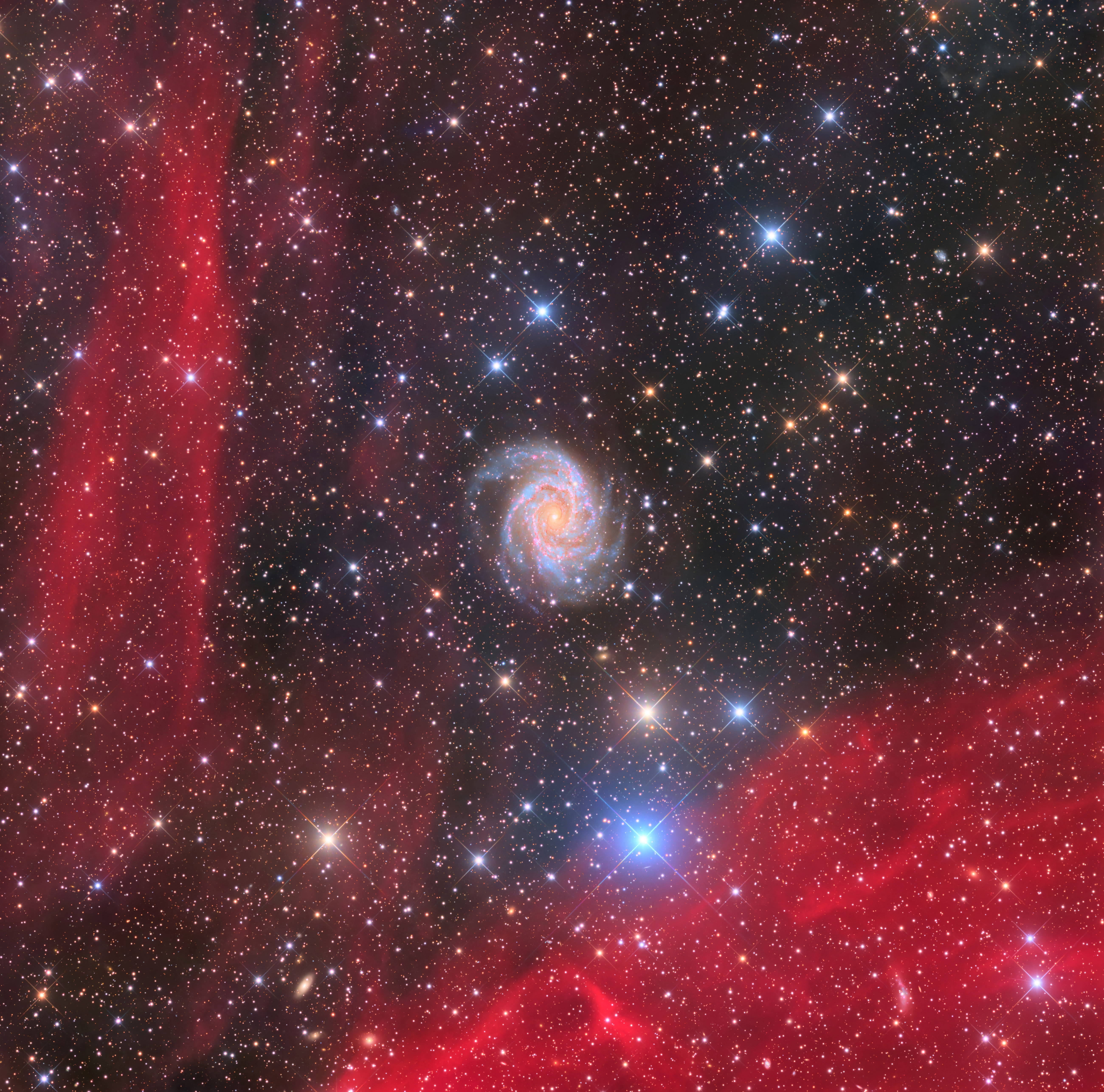 A spiral galaxy is seen behind red clouds of dust in space