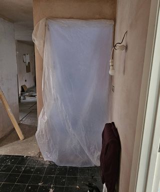 freshly plastered hallway with black floor tiles and plastic sheeting surrounding doorway