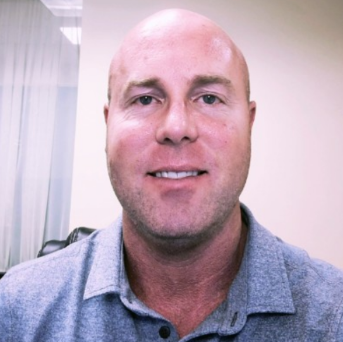 Todd is a white man with shaved down hair and is pictured wearing a gray polo shirt