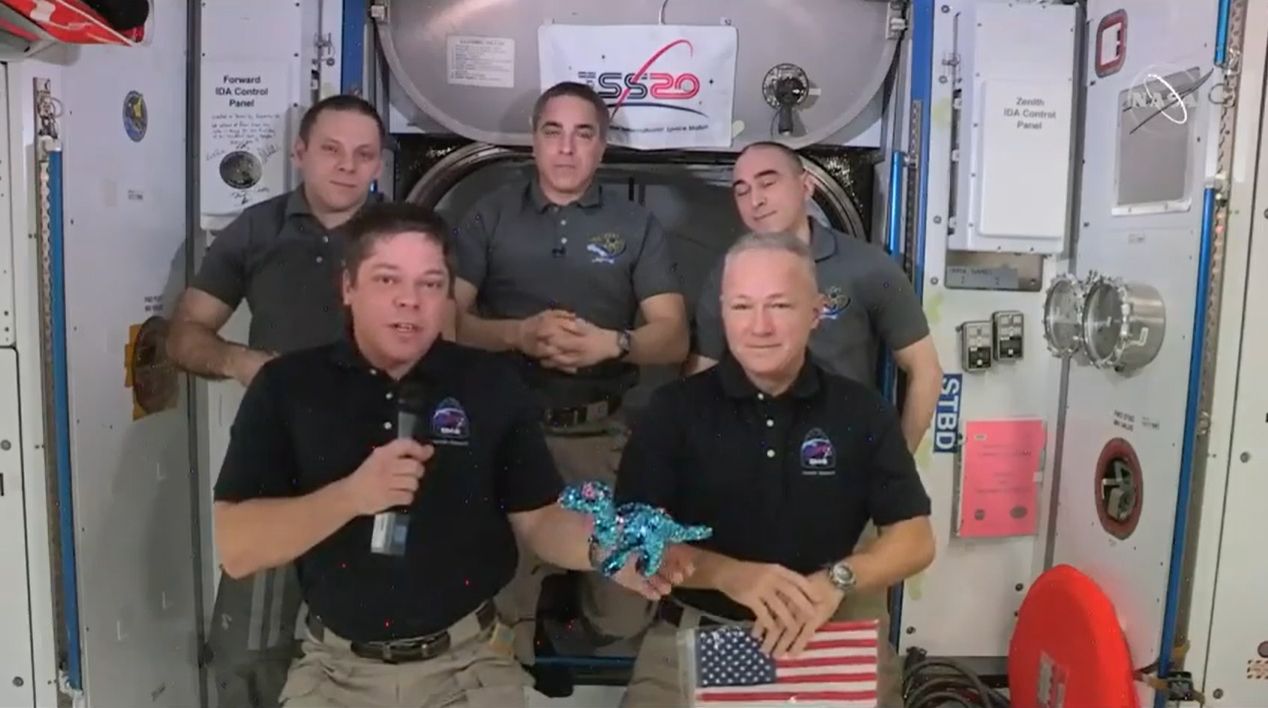 NASA astronaut Bob Behnken displays Tremor the apatasaurus, a toy dinosaur that he and Doug Hurley brought with them on SpaceX's Demo-2 Crew Dragon test flight to serve as a weightless indicator, during a farewell ceremony on the International Space Station Aug. 1, 2020.
