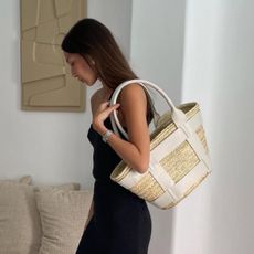 Woman wears black dress and carries DeMellier basket bag