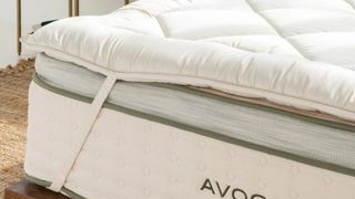 Avocado mattress topper deals and sales: image shows the Avocado Green mattress topper tied to a corner of an Avocado mattress to make the bed softer