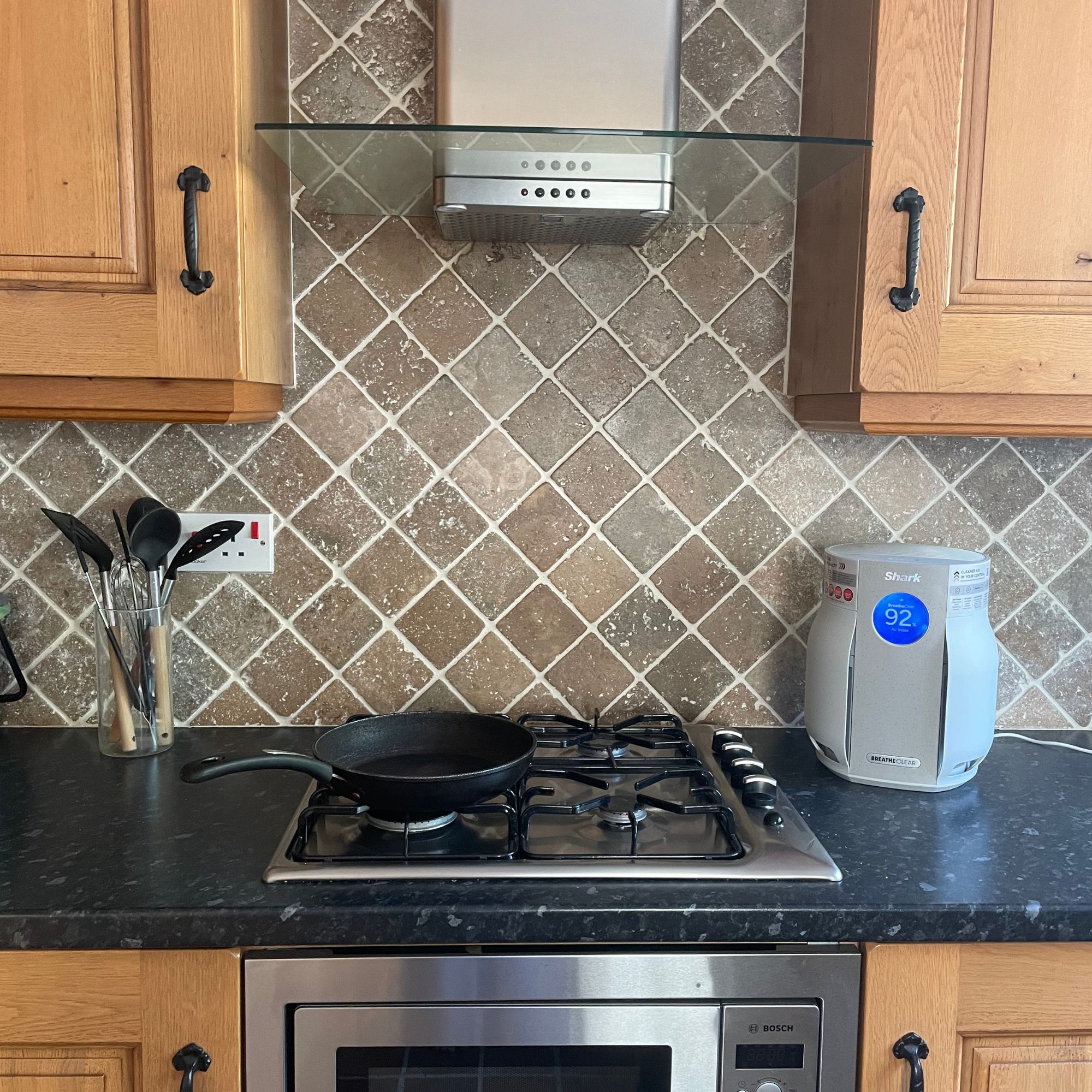 Shark BreatheClear Compact Air Purifier with NeverChange6 sitting on the counter of a brown kitchen with black worktops and a frying pan on the hob