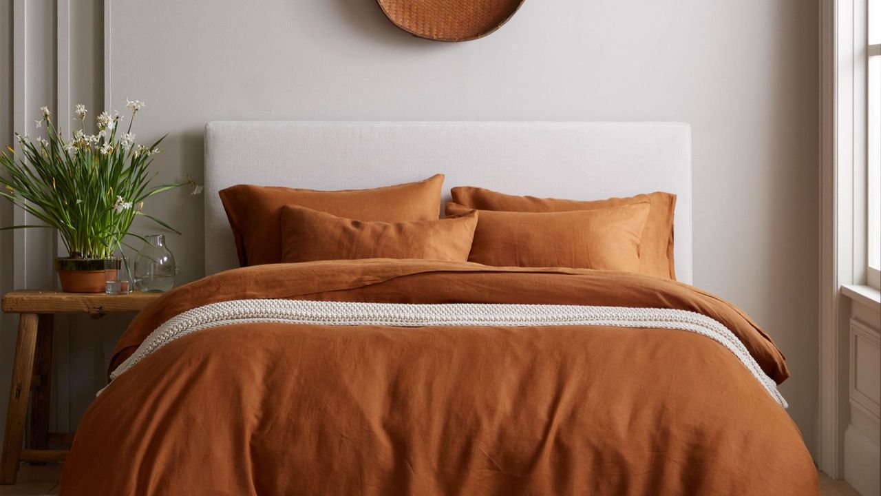 Orange and white sheets and pillows on a white bed against a white wall. 