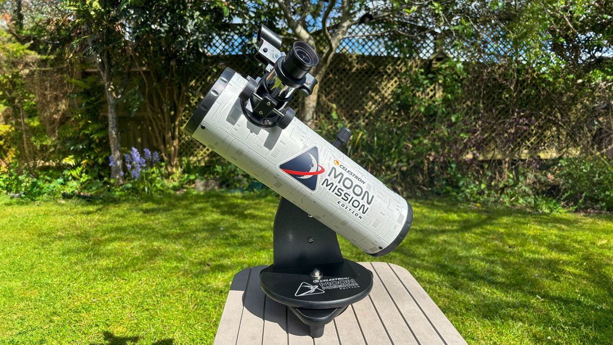 The Celestron Moon Mission 100mm Tabletop Dobsonian on a grey table with grass and trees in the background.