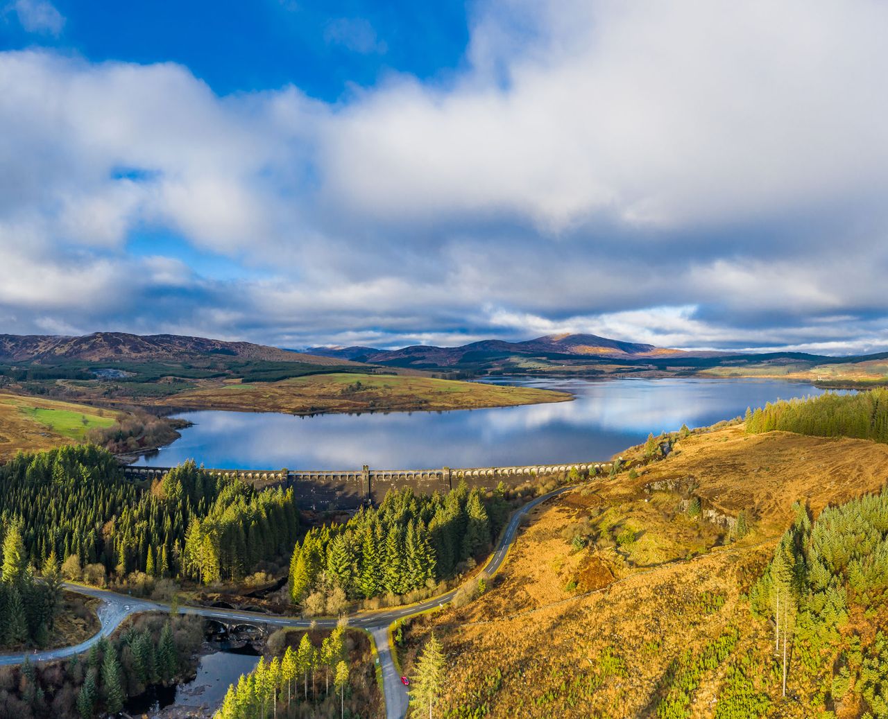 A panoramic aerial view, captured by a drone, of a fresh water reservoir created by building a dam across a Scottish river. The dam was part of the Galloway hydro electric scheme which was built between 1930 and 1936. The loch is in part of the country popular for walking and mountain biking. The panorama was created by merge several images together.