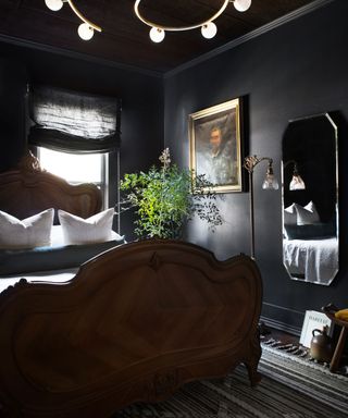 Mirror at the foot of bed in dark bedroom space with wooden accents and greenery near window