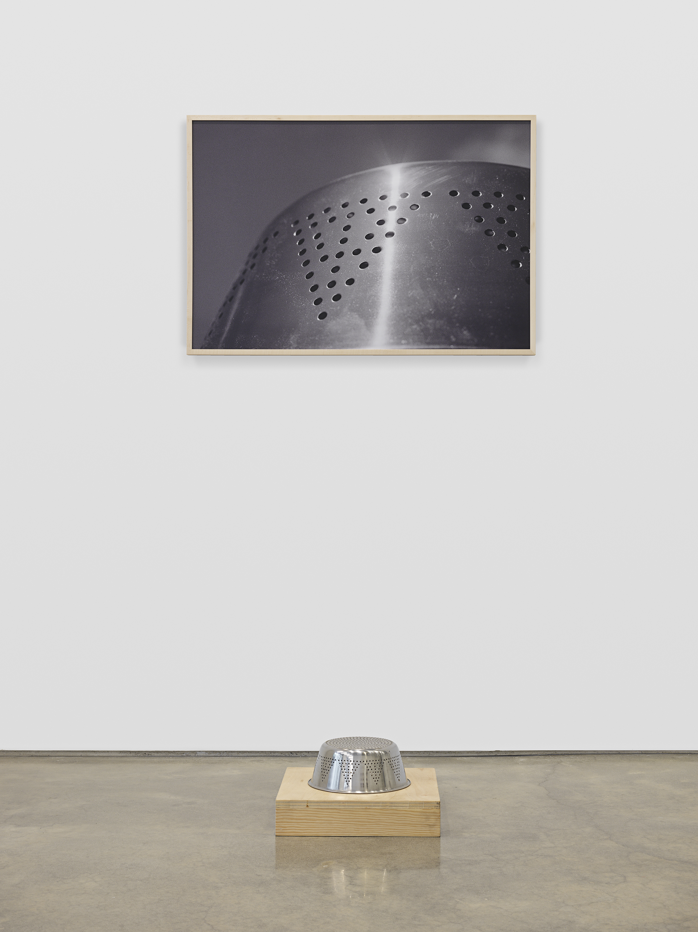 metal colander on low plinth and print of the object on a wall