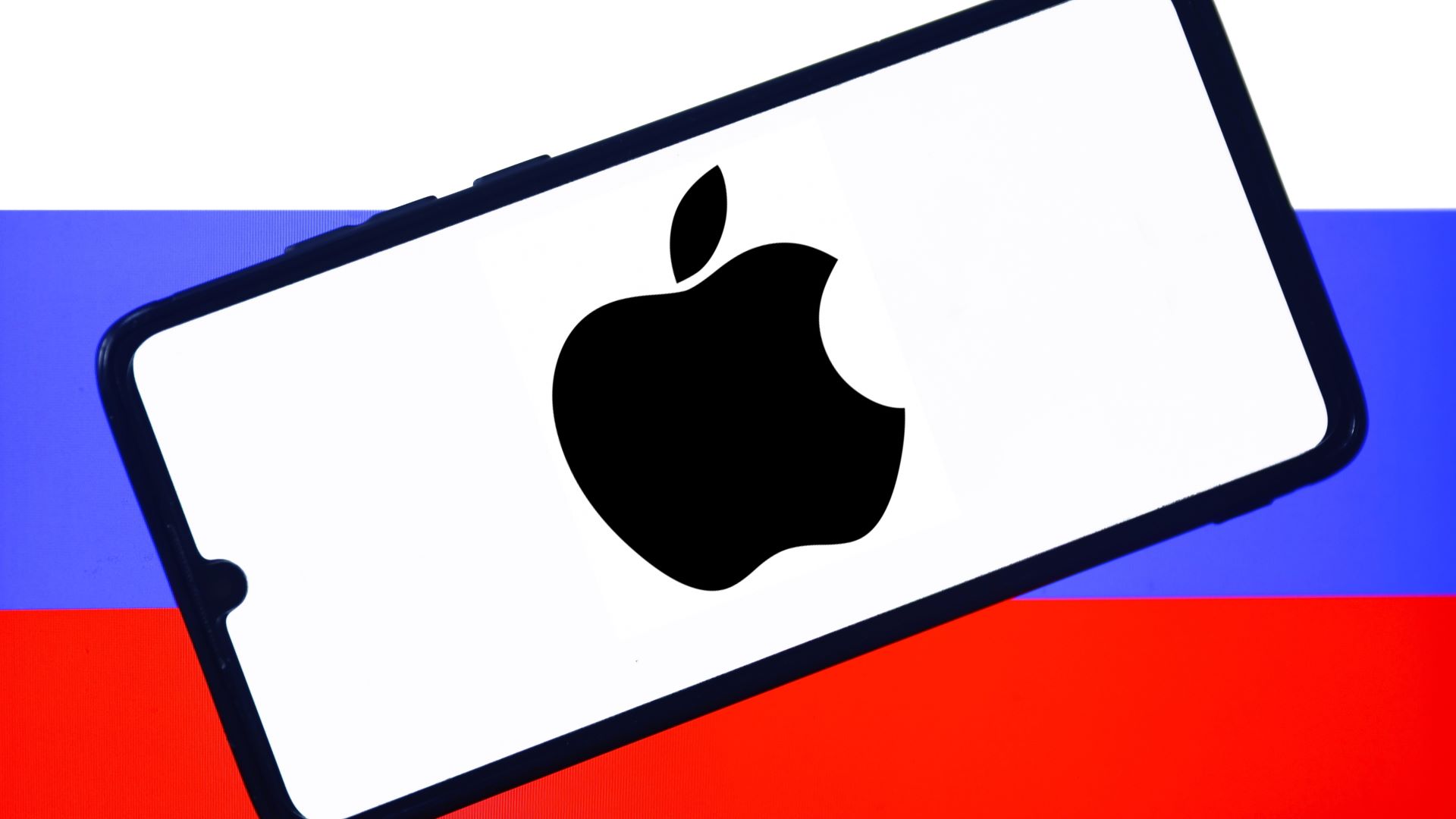 Apple logo is displayed on a mobile phone screen photographed with Russian flag in the background for the illustration photo taken in Poland on July 19, 2022.