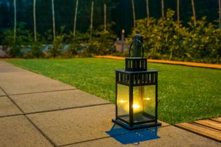 Portable lantern on the edge of a garden patio and path