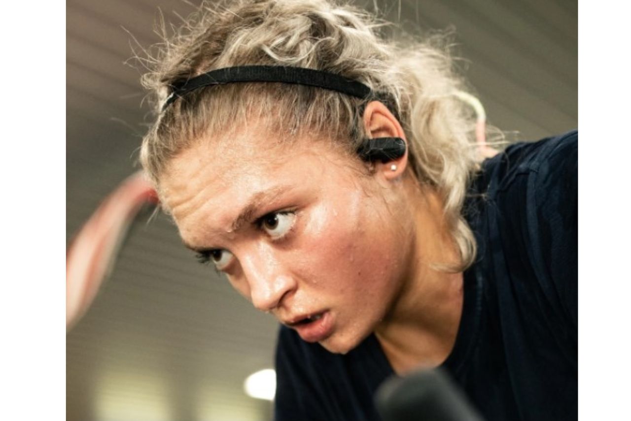 This image is showing a womans head and face. She is sweating lots, in her ears are a pair of ESC Sounds headphones, they are one of the best headphones for cycling