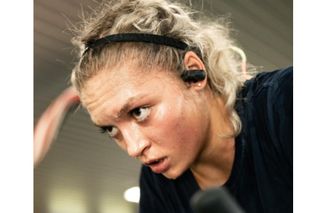 This image is showing a woman's head and face. She is sweating lots, in her ears are a pair of ESC Sounds headphones, they are one of the best headphones for cycling
