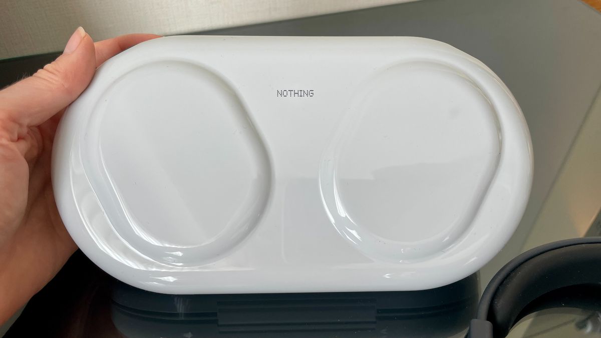 Nothing Headphone (1) Pro with the case on a shiny black and glass table, held in a hand