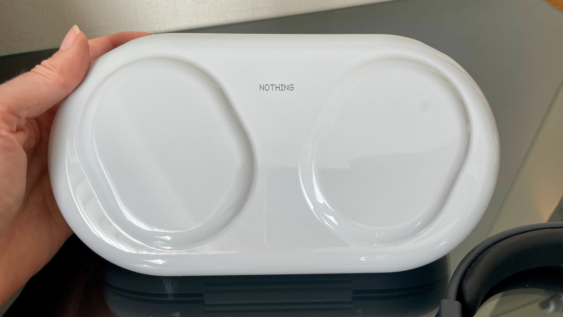 Nothing Headphone (1) Pro with the case on a shiny black and glass table, held in a hand
