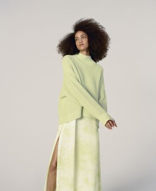 an everlane model wears a green sweater with a coordinating tie-dye skirt