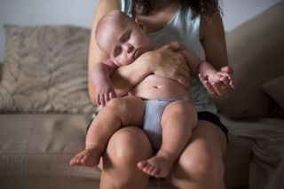 Baby asleep on mum's lap on sofa downstairs