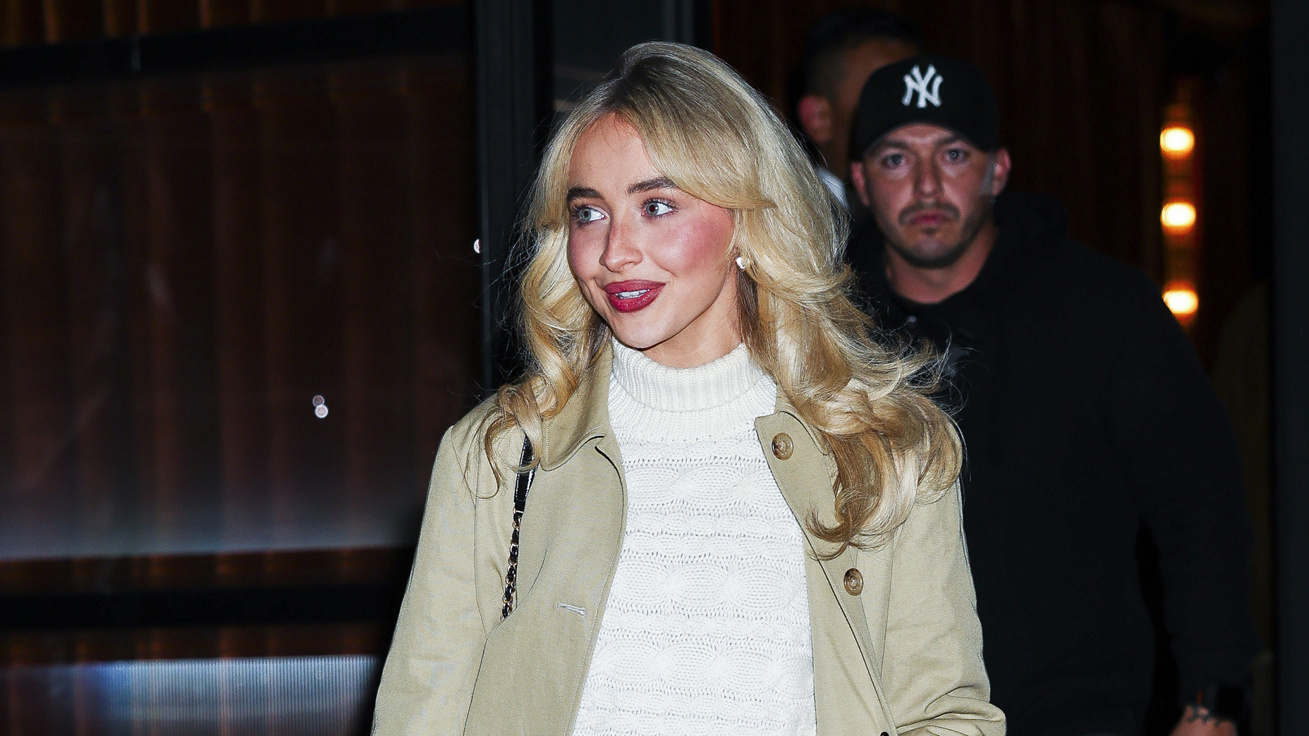 Sabrina Carpenter wearing a tan trench, cream sweater, and black miniskirt out to dinner with Taylor Swift