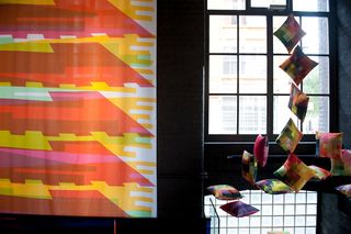 Left: Colourfully designed curtain hanging against a black background. Right: Colourful pillow cushions hanging from the ceiling with a glass window in the background