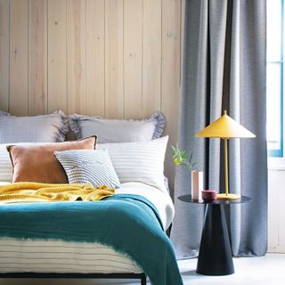 Bedroom with colourful bedding, bedside table, table lamp, and grey curtains