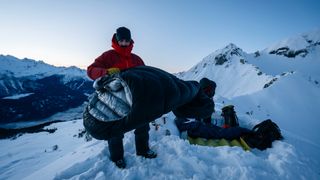 Man high on mountain ridge with sleeping bag