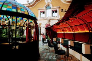 A Roman terrace complete with a colorful glass pavilion and semi-covered curtain dining area exudes a quirky, eccentric feel.