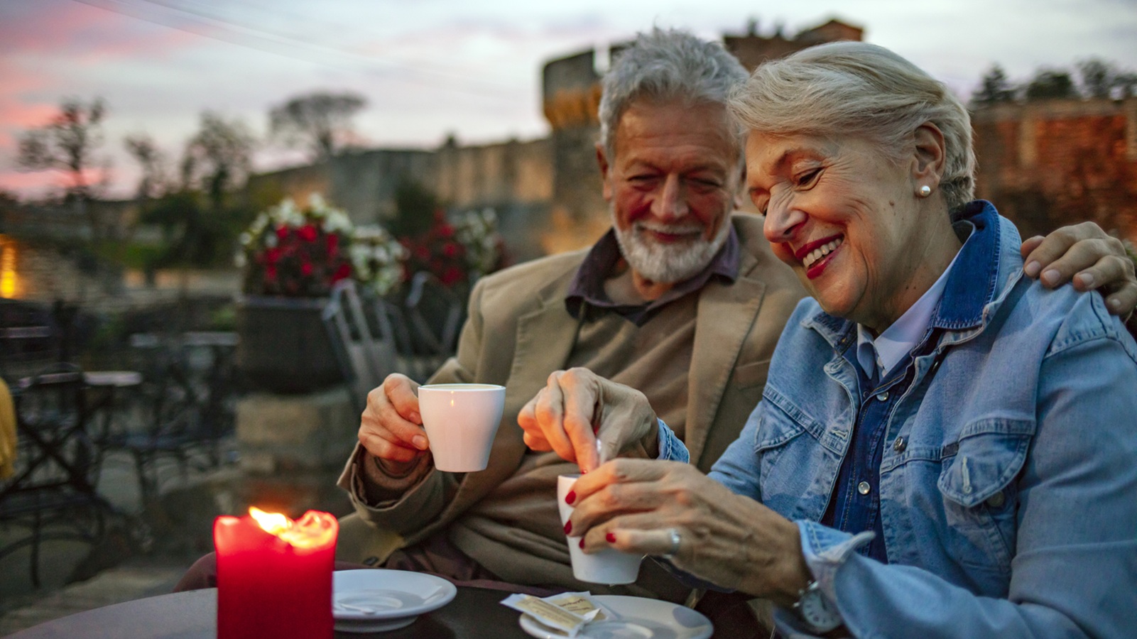 Senior Couple Enjoying Cup Of Coffee In in luxury rooftop restaurant at sunset during autumn day.