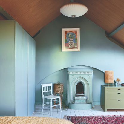 A soft blue colour drenched bedroom with painted floorboards and an arched wooden ceiling