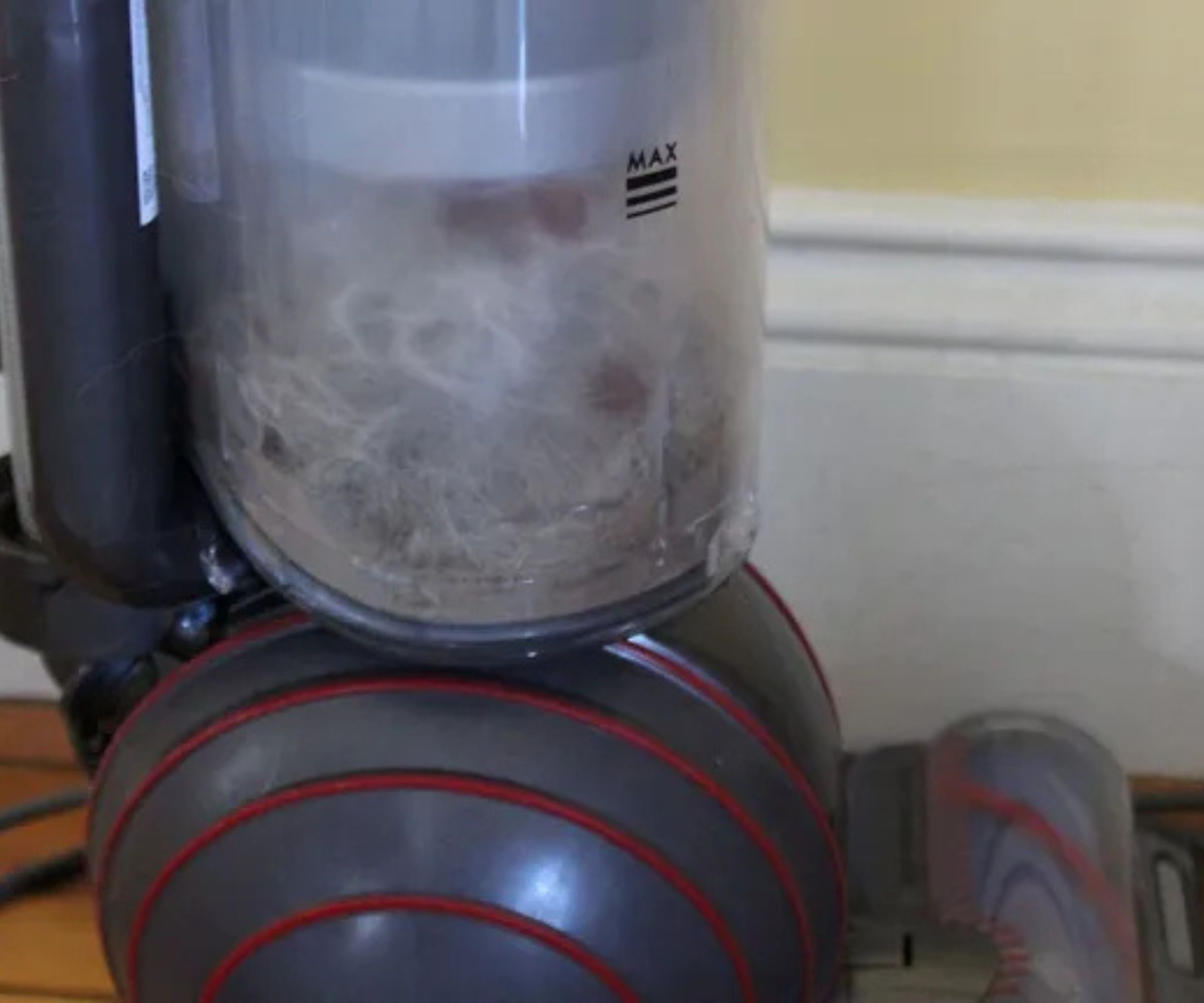 Closeup of the Dyson Ball Animal 3 upright vacuum's dustbin full of dust and pet hair in Camryn Rabideau's home, with cream baseboards and wooden floor pictured behind.