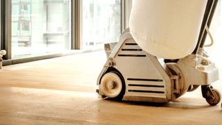 Close up of belt sander sanding light wooden floor 