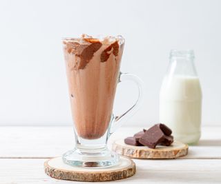 A coffee smoothie in a glass with milk and chocolate in the background