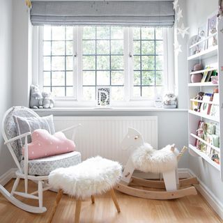 Nursery with wooden floor, light grey walls with cloud motif, white crib, rocking chair and horse in window alcove.