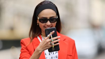 Woman in a red blazer and a black headband with her phone in one hand in focus