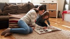 A mother and daughter looking through a photo album on the living room floor