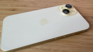 A yellow iPhone 15 on a wooden desk