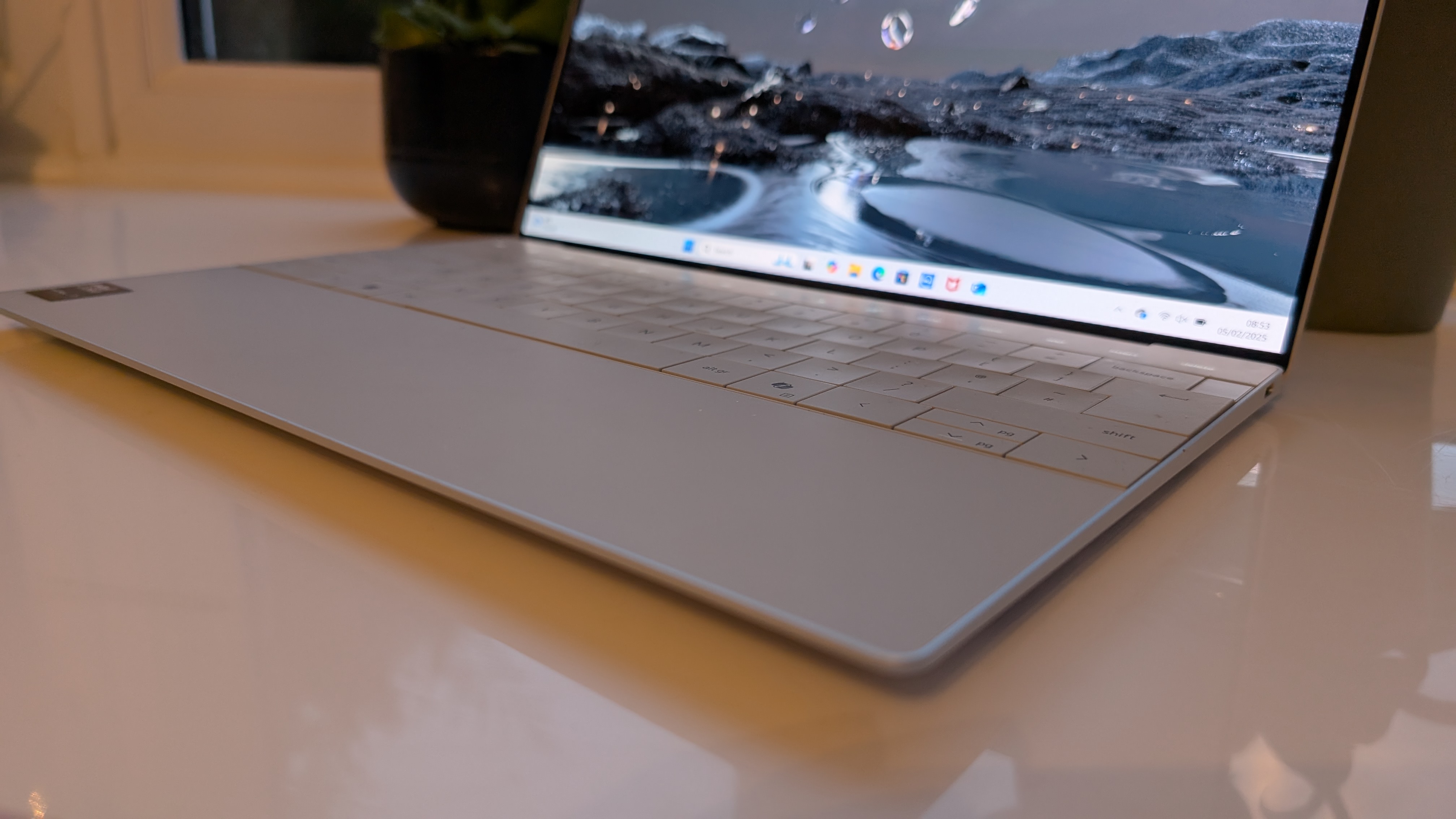 The Dell XPS 13 pictured on a white surface in front of a window with two potted plants.