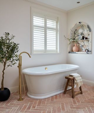 modern bathroom with terracotta floors and window shutters over a freestanding bath