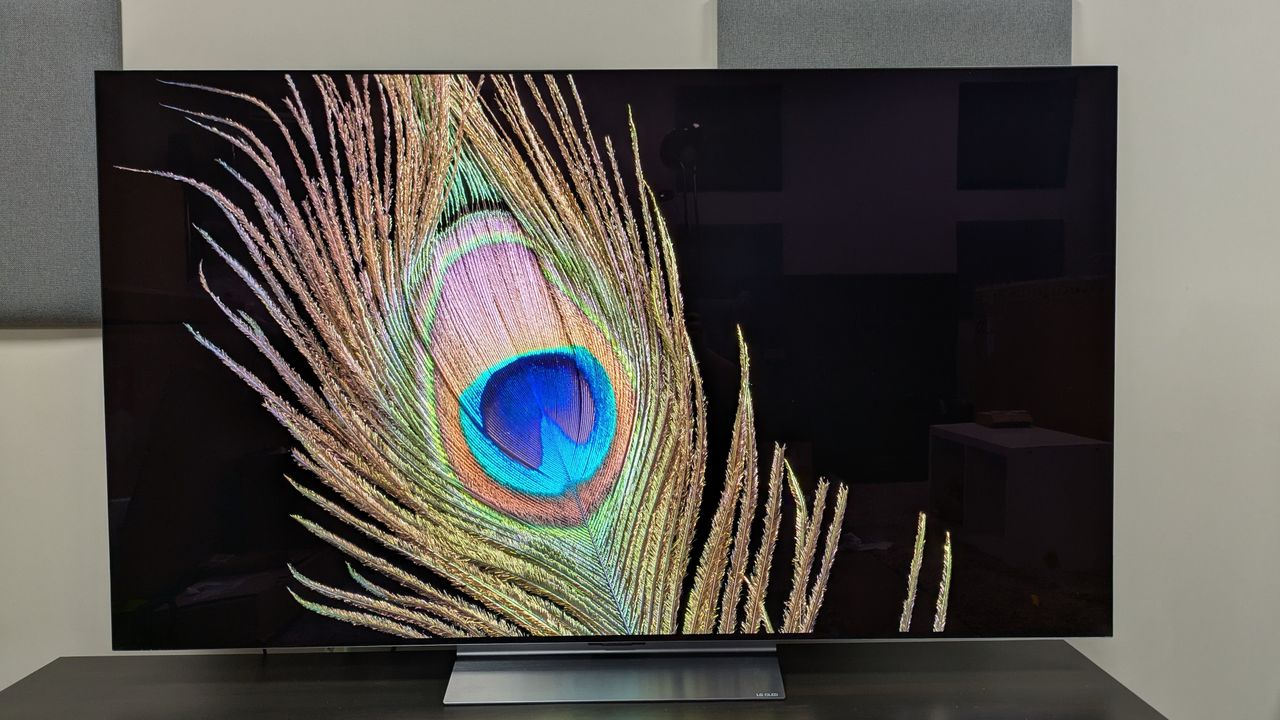The LG C6 OLED TV with a peacock feather against a black background on screen. The peacock feather is detailed and the background is a deep black, but some reflections from the room are visible.