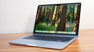 Apple MacBook Air 13-inch M4 on a wooden table with the display showing the macOS Sequoia desktop.