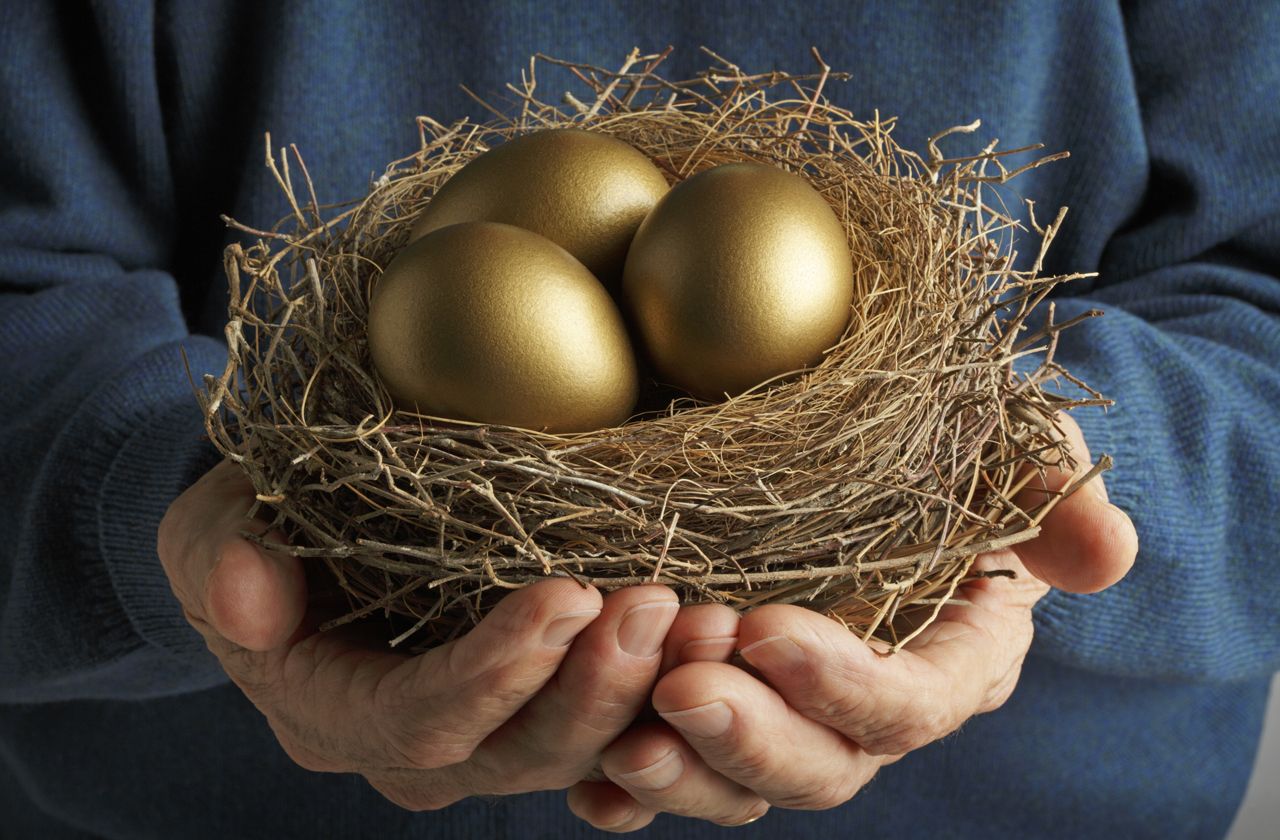 Senior Citizen holding three golden eggs in a bird&amp;#039;s nest.