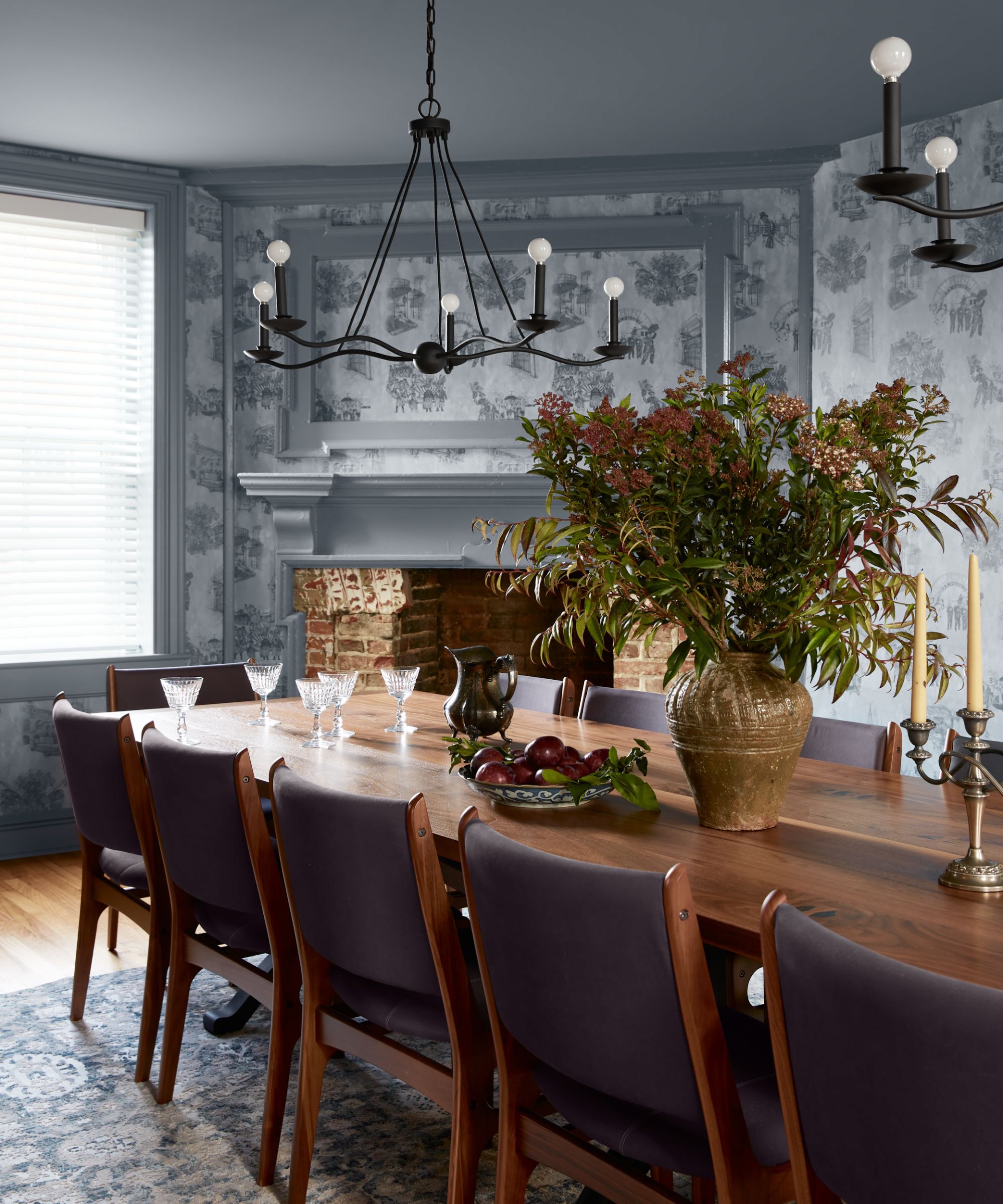 A dining room with gray patterned wallpaper, gray trimwork, a large wooden dining table, and gray chairs.