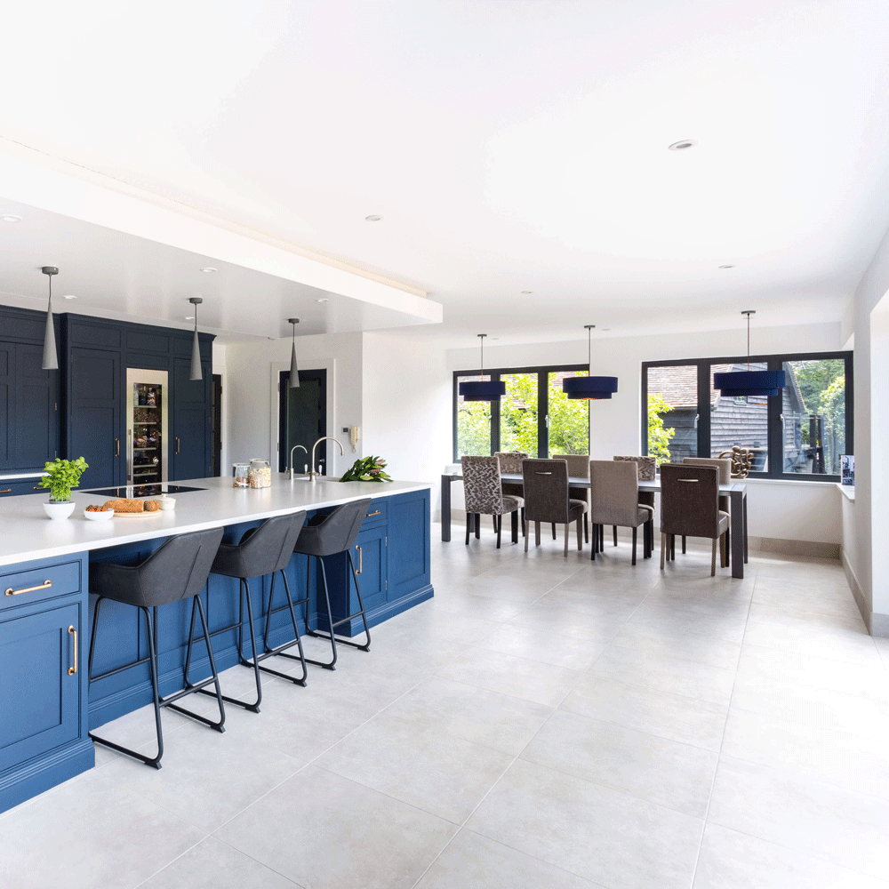 White tiled open plan kitchen with blue cupboards and a dinning table with chairs