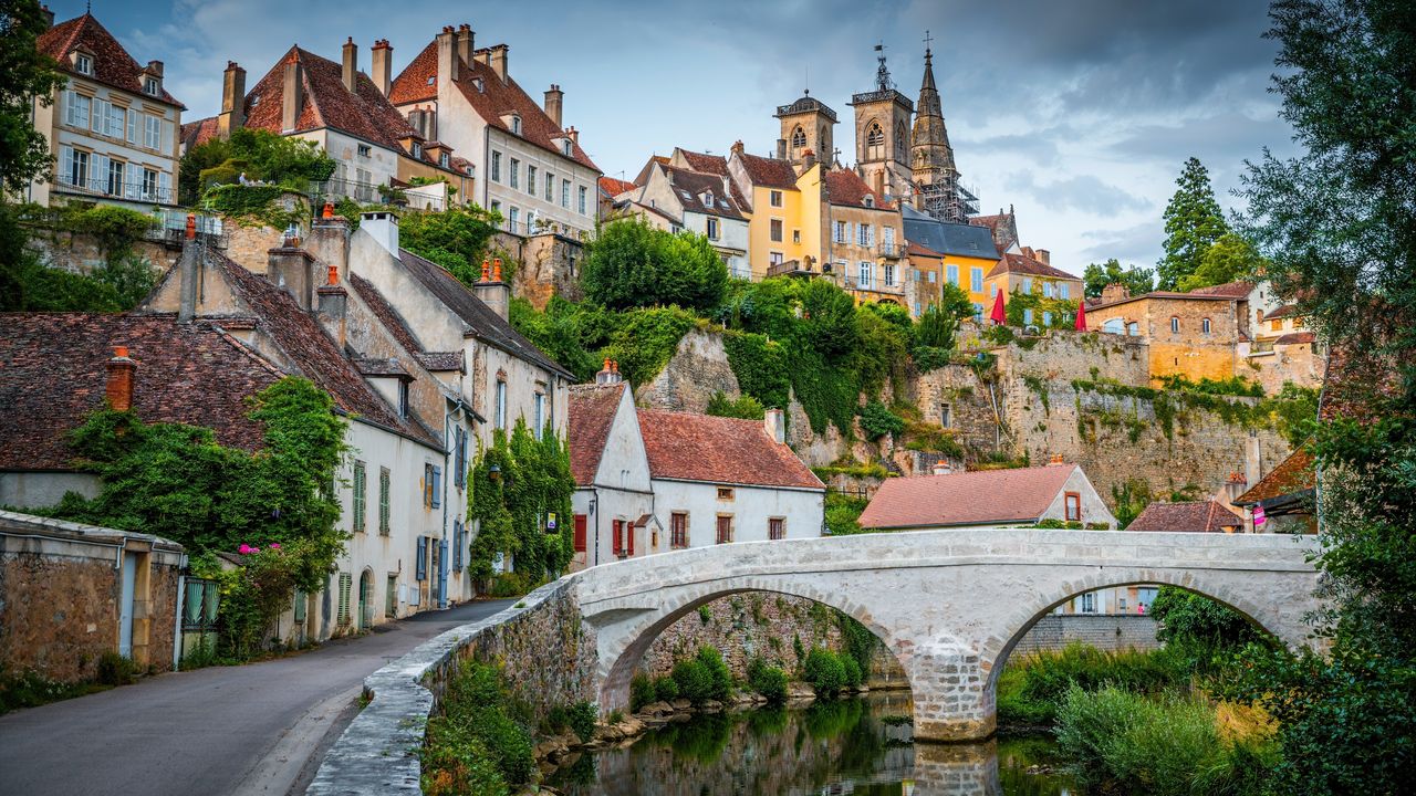 An old stone bridge crossing a river in the foreground and stone, French houses in the background