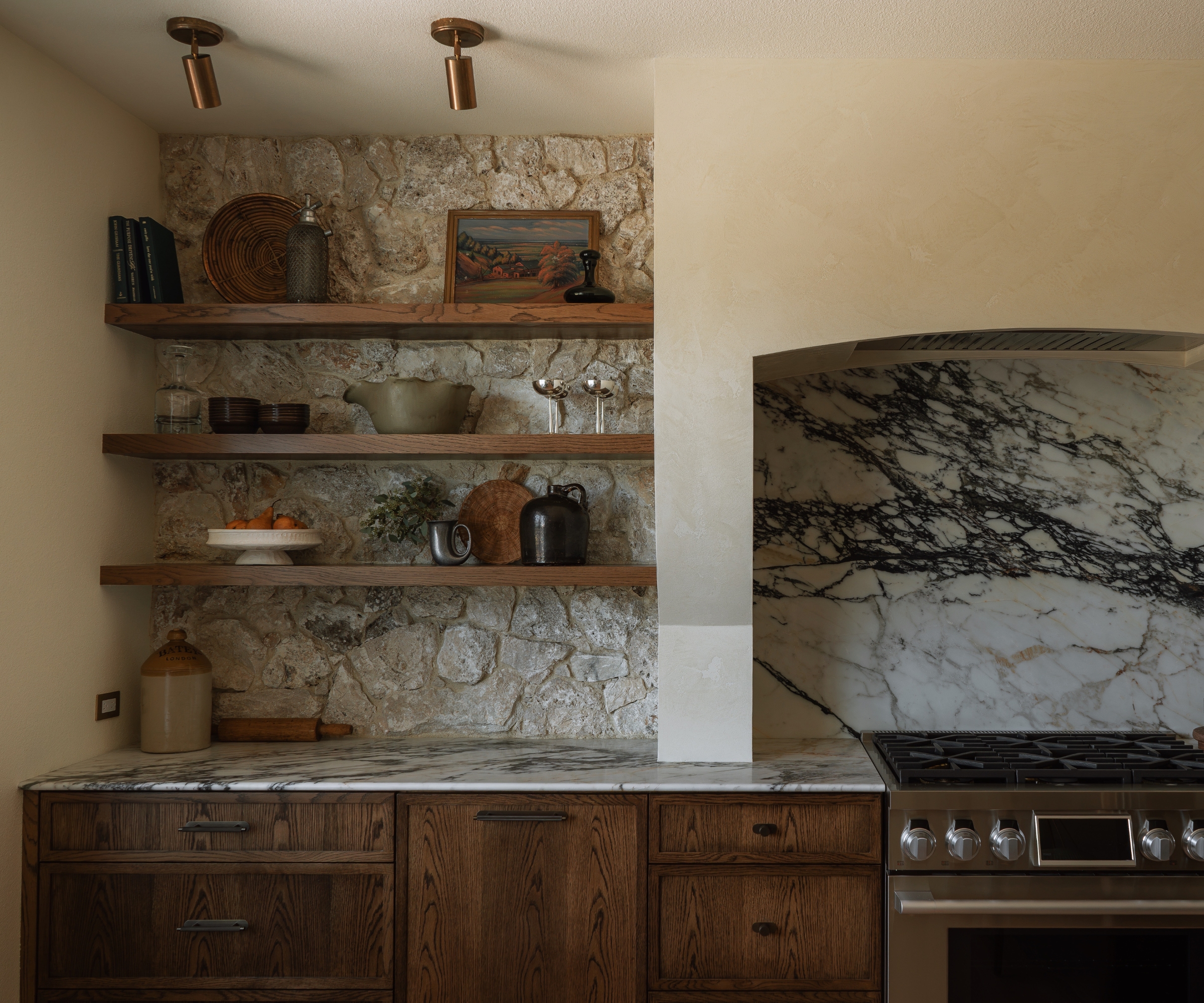 a dark wood kitchen with warm white walls, wooden open shelving, and a mic of warm and cool toned metals