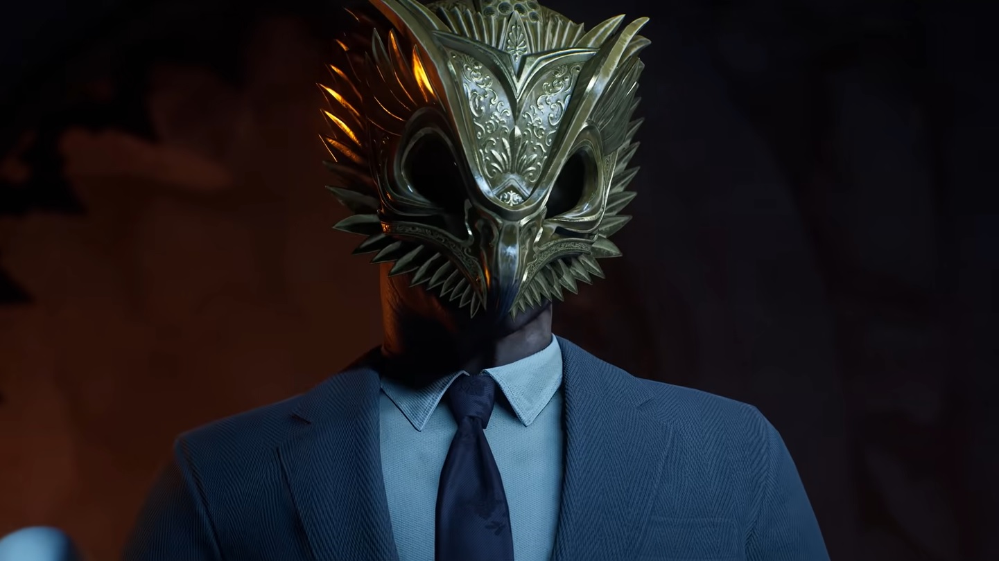 Gotham Knights - A person in a suit and tie wearing a golden face mask that looks like an owl's head