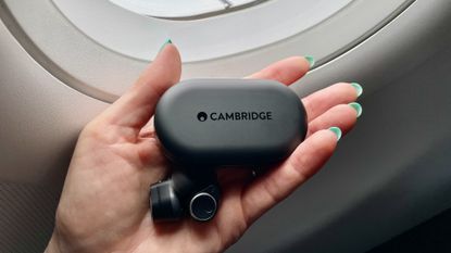 Cambridge Audio Melomania M100, held in a hand with blue fingernails, in the window of an aircraft