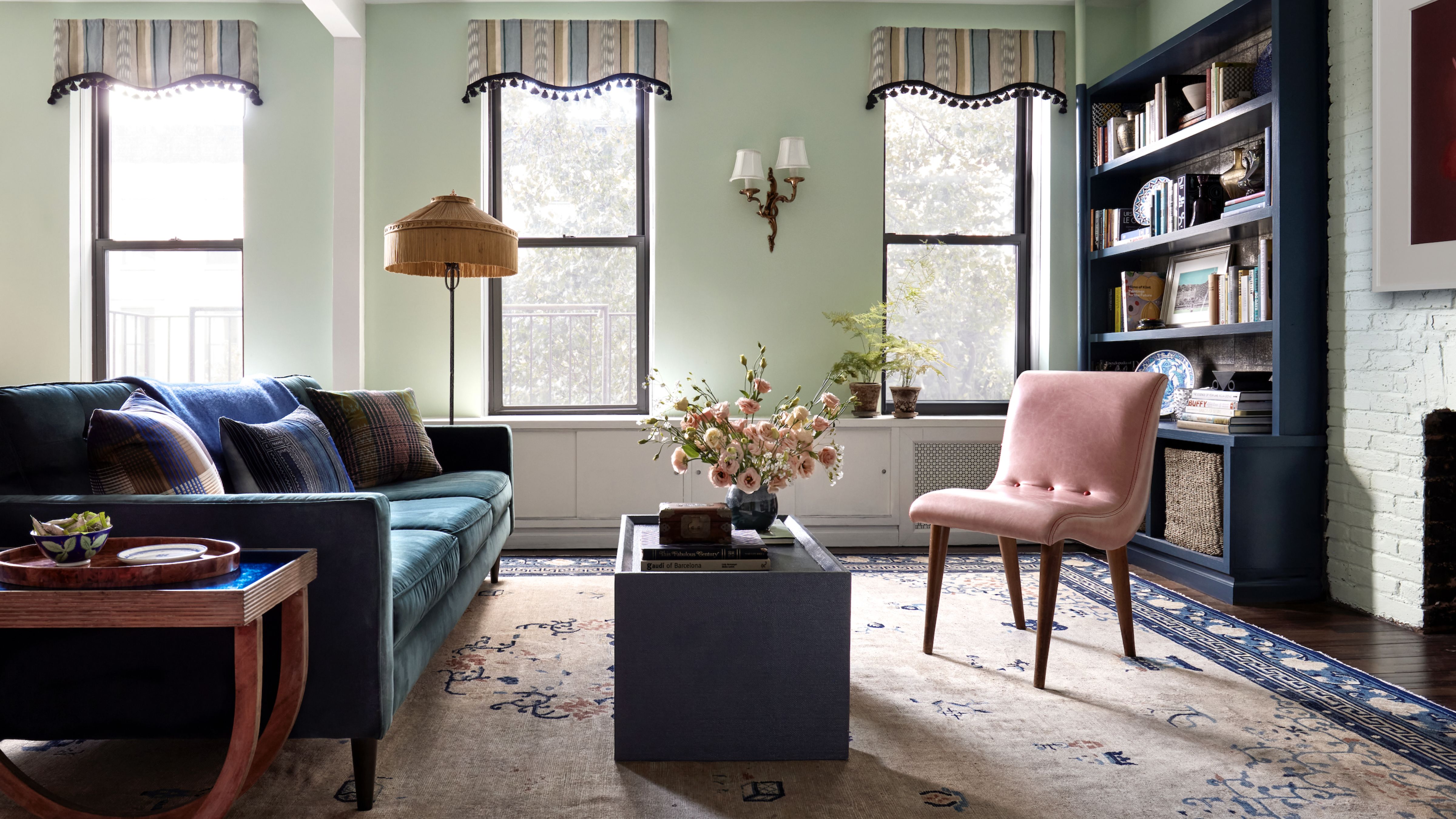Light green NYC living room styled with a teal rug, rectangular coffee table, pink accent chair, and striped curtain valences